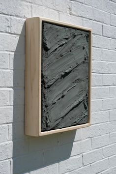 a white brick wall with a wooden frame hanging on it's side next to a black stone block