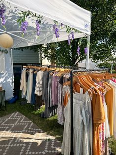 an outdoor clothing rack with clothes hanging from it's sides and purple flowers on the top