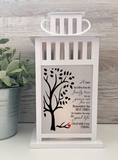 a small white lantern with a tree and poem on it next to a potted plant