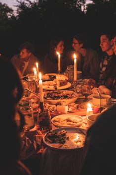 a group of people sitting around a table with food and candles in front of them