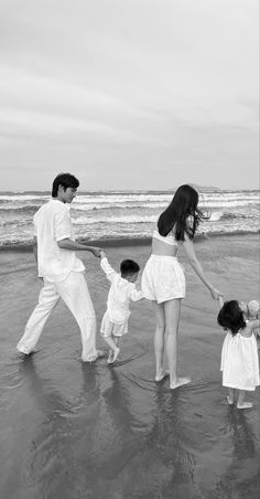 a family playing on the beach in black and white with one child holding his mother's hand