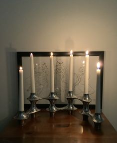 five lit candles sit on a wooden table in front of a framed photo with the drawing beauty and the beast behind them