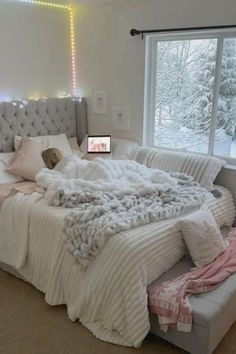 a bedroom with a large bed and lots of blankets on the top of it, next to a window