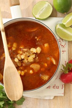 a wooden spoon sitting in a bowl filled with soup next to limes and strawberries