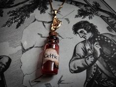 "Celtic Blood" - Necklace .Small pendant of a vial of Celtic blood, decorated with a chain and a Harp charm, from vintage recycled jewelry. Features a small burnt effect label reading "Celtic Blood". Fake blood made from physiological serum and VFX liquid, filling half of the vial. Vial sealed with UV resin. .Small pendant of a Celtic blood vial, decorated with a chain and a Harp charm, from vintage recycled jewelry. Has a small burnt effect label with the words "Celtic Blood. Fake blood designe Blood Necklace, Map Making, Recycled Jewelry, Fantasy Map, Small Pendant, Uv Resin, Harp, Necklace Etsy, Jewelry Necklace Pendant