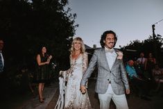 a man and woman walking down the street holding hands with people in the back ground