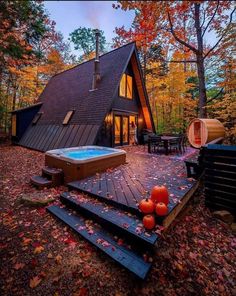 an outdoor hot tub in front of a house with fall leaves on the ground and trees surrounding it