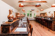 a long table with lots of copper pots on it in a room filled with wooden tables and chairs