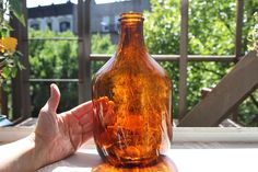 a person holding their hand up to a brown glass bottle with orange liquid inside it