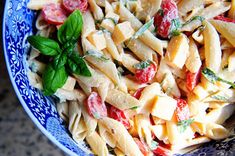 a blue and white bowl filled with pasta, tomatoes and basil garnished with parsley