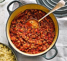 a large pot filled with food next to two smaller bowls full of rice and spoons