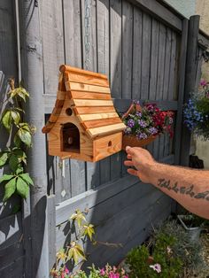 a person holding a bird house with flowers in the background