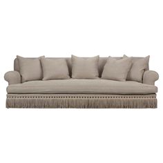 a beige couch with fringe trimmings and pillows on the back, against a white background