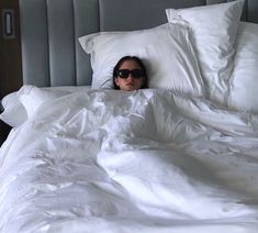 a woman laying in bed with her head under the covers and eye glasses on top