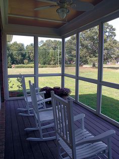 four white rocking chairs on a porch with grass and trees in the backgroud