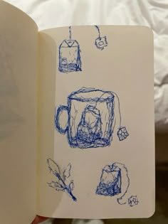 an open book with blue ink drawings on the pages and inside it is a coffee mug