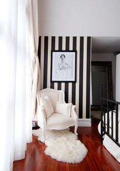 a white chair sitting on top of a hard wood floor next to a black and white striped wall