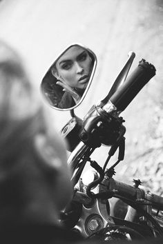 black and white photograph of a woman looking in the side mirror of a motorbike