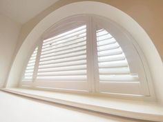 an arched window with white shutters in the corner