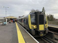 a yellow and black train pulling into a station with people waiting on the platform to board