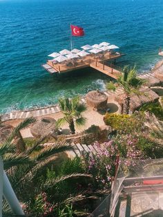 a dock with chairs and umbrellas in the water next to some palm trees,