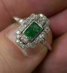 a woman's hand holding an emerald and diamond ring