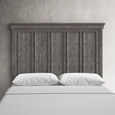 an upholstered bed with white pillows and wooden headboard against a gray wall