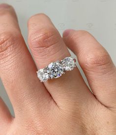 three stone diamond ring on someone's hand, with the middle one in white gold