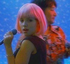 a woman with pink hair is standing in front of a microphone and another man behind her