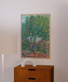 a painting is hanging on the wall above a dresser with a white lamp next to it