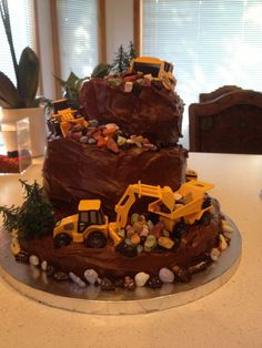 a three tiered chocolate cake with construction vehicles on top and rocks around the base