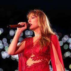 a woman in a red dress holding a microphone and singing into the air with lights behind her