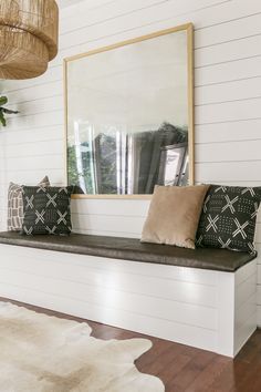 a bench with pillows and a mirror on the wall above it in a white room