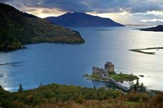 a castle sits on an island in the middle of a body of water surrounded by mountains