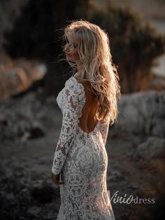 a woman in a white dress is standing on some rocks and looking back at the camera