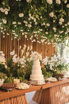 a wedding cake sitting on top of a wooden table covered in flowers and greenery