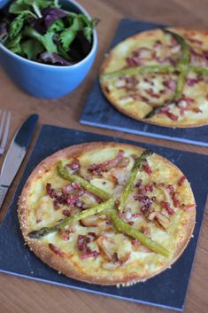 two small pizzas sitting on top of blue placemats next to a salad