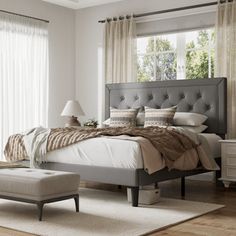 a bedroom with a bed, ottoman and window in the corner next to a chair