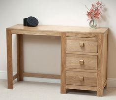 a wooden desk with three drawers and a vase on the top, against a white wall