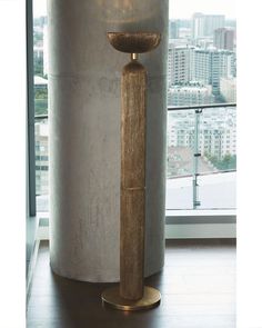 a tall wooden candle holder sitting in front of a window next to a large metal cylinder