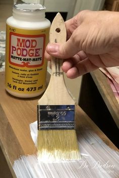 a person holding a paint brush near a bottle of mod podge