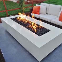 a fire pit sitting on top of a patio next to a white couch and orange pillows