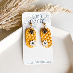 a pair of earrings with bees and honeycombs on them sitting on a white plate