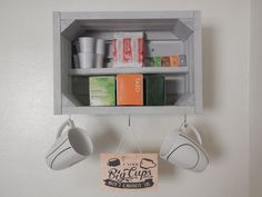 a shelf with cups hanging from it's sides and two mugs hanging on the wall