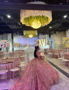 a woman in a pink ball gown sitting at a table with chairs and chandeliers