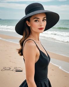 a woman in a black dress and hat on the beach