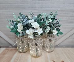 four glass vases with flowers and greenery in them sitting on a wooden table