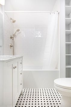 a white bathroom with black and white floor tiles on the shower, toilet and bathtub