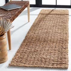 a rug on the floor next to a table with a laptop and plant in it