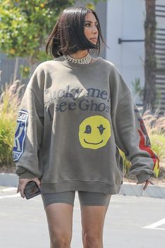 a woman walking down the street wearing a sweatshirt and shorts with an embellished smiley face on it